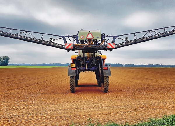 Traktor fährt über ein Feld mit seitlich ausgefahrenen Armen