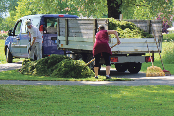 Zwei Personen laden Gartenabfälle auf einen Auto-Anhänger